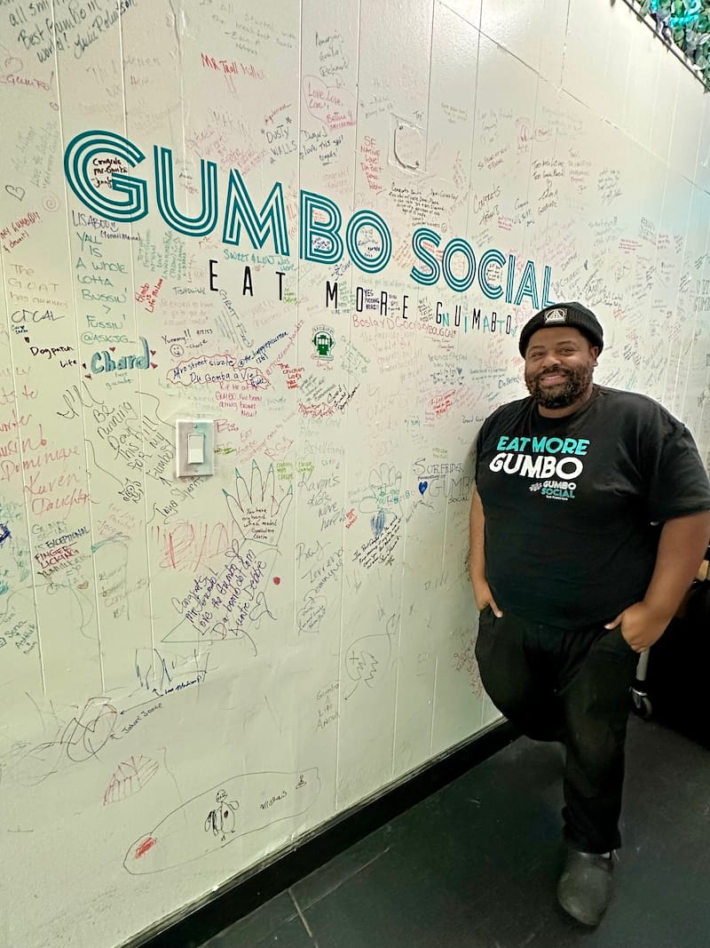 Gumbo Social’s chef-owner Dontaye Ball at the wall of notes from friends and customers. 