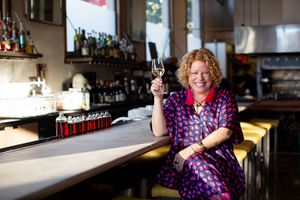 Marcia Gagliardi sitting at the bar at NOPA restaurant holding a glass of Champagne.